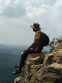 Side view of man sitting on rock against sky