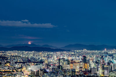 High angle view of illuminated city against blue sky