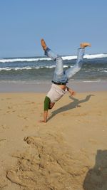 Mid adult man doing handstand at beach against clear blue sky during sunny day