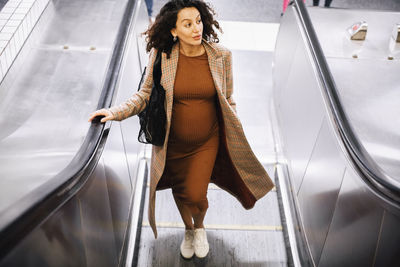 Pregnant businesswoman looking away while moving upon escalator at station