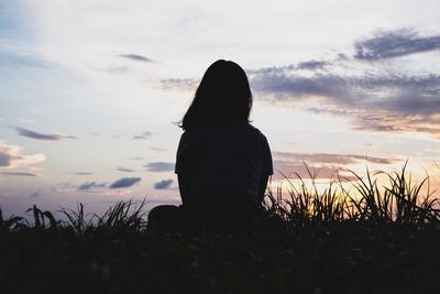 Rear view of woman sitting on field against sky during sunset