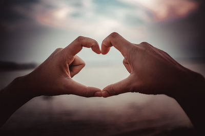 Cropped hand of man making heart shape against beach