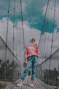 Man standing on footbridge against sky