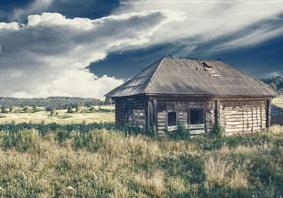 Old house on field against cloudy sky
