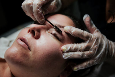 Crop anonymous cosmetician in latex gloves curling eyelashes of female patient during lash lift procedure in salon