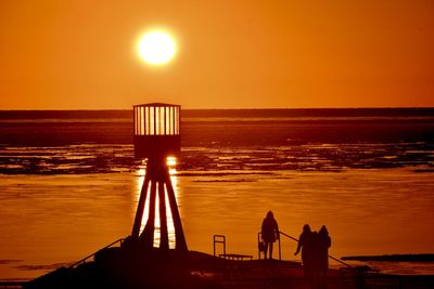 Silhouette people looking at sea against sky during sunset