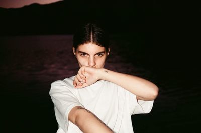 Portrait of young woman standing against black background