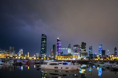 Illuminated buildings by river against sky at night