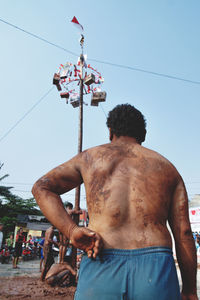 Rear view of shirtless man standing against the sky