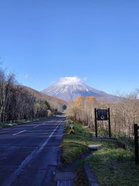 Road leading towards mountain against blue sky