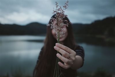 Woman holding plant against lake
