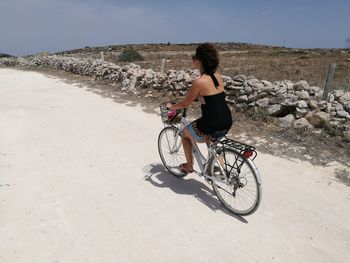 Full length of woman riding bicycle on dirt road