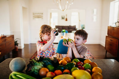 Young boy and girl sitting at kitchen counter with fruits and veggies