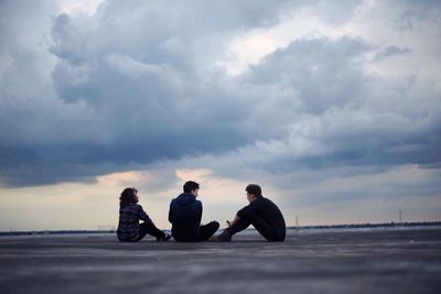 Men sitting on beach against sky