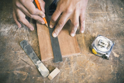 Cropped hands of carpenter marking with pencil on wooden plank at workshop