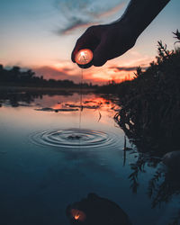 Reflection of silhouette person hand in lake against sky during sunset