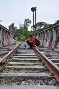 Man sitting on railroad track against sky