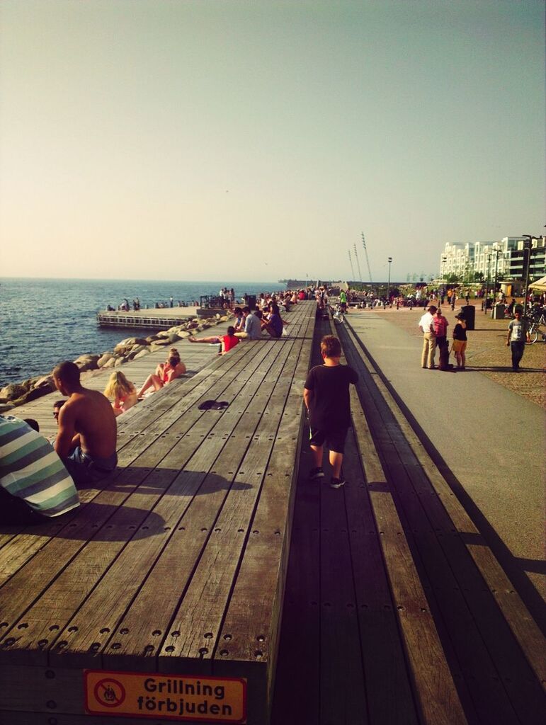 sea, large group of people, clear sky, men, water, copy space, person, lifestyles, horizon over water, beach, leisure activity, transportation, sky, tourist, mixed age range, tourism, travel, built structure, outdoors