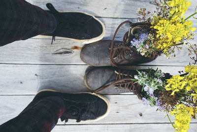 Low section of man standing by flowers in boots on floorboard