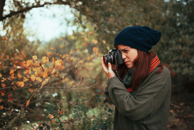 Woman photographing with camera while standing in forest