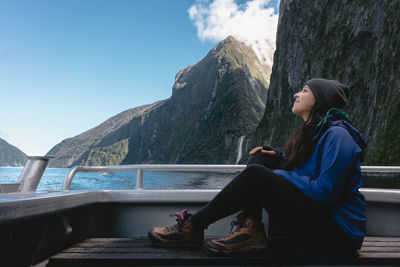 Man sitting on mountain by lake against sky