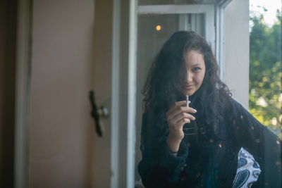 Portrait of woman smoking cigarette by window at home