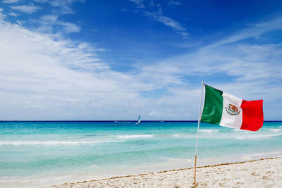 Mexican flag on beach against blue sky