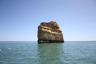 Scenic view of rock formation in sea against clear blue sky