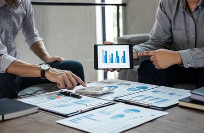 Midsection of businessmen discussing over graph in digital tablet at office