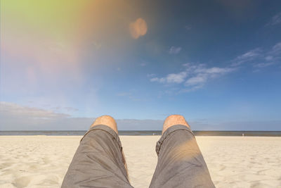 Low section of man at beach against sky