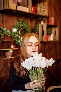 Young woman smelling flower at home