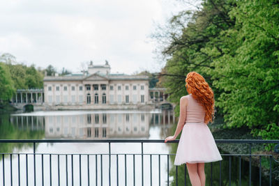 Rear view of woman standing by railing against trees