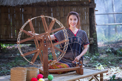Young woman weaving thread on wheel against house