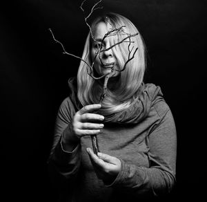 Portrait of woman covering face with plant against black background