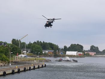 Helicopter flying over river in city against sky