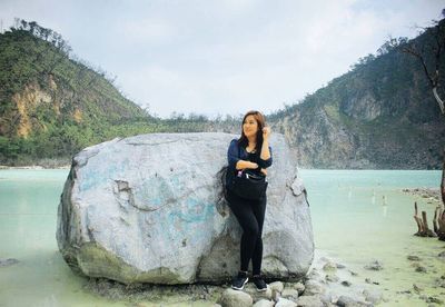 Portrait of young woman standing on rock against sky