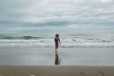 Child running on beach against sky