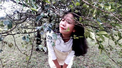 Young woman standing by tree against plants