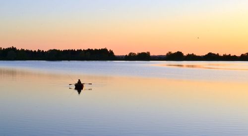 Silhouette man on boat in lake against sky during sunset