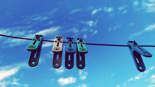 Low angle view of clothespins hanging on rope against sky