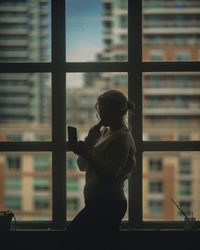 Side view of silhouette woman looking through window