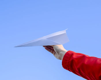 Cropped image of hand holding paper airplane against clear blue sky