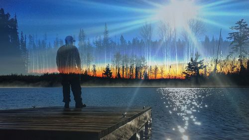 Rear view of silhouette man standing by lake against sky at sunset