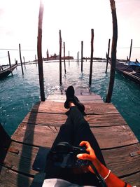 Low section of woman holding camera while sitting on pier