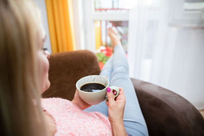 A blonde woman holds a cup of coffee while sitting in a chair.