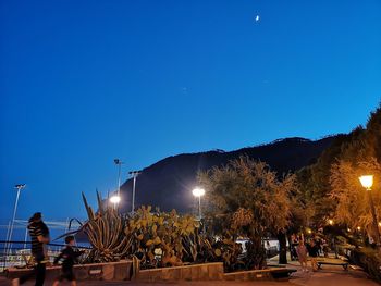 People on illuminated street lights against blue sky at night