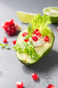 Halved avocado with cream cheese, pomegranate seeds, lettuce, mint and lime.