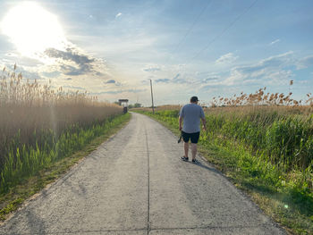 Rear view of person walking on road amidst field against sky