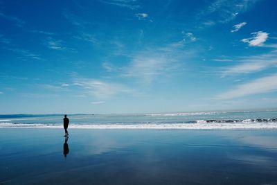 Silhouette man on shore at beach against blue sky