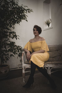 Young woman sitting on chair against wall